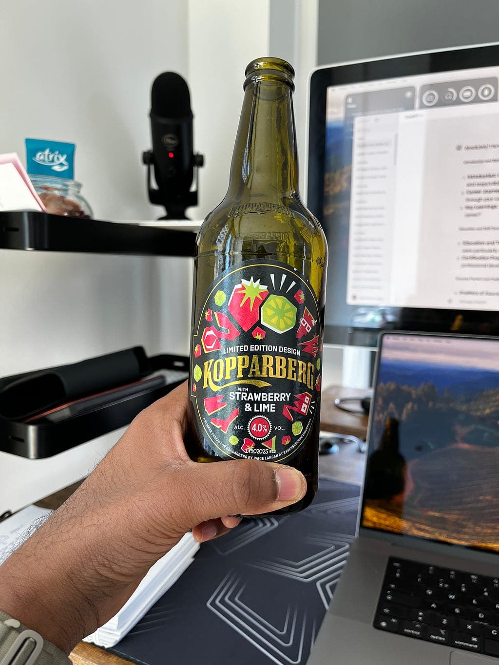 A fruit drink beside a laptop and microphone on a desk